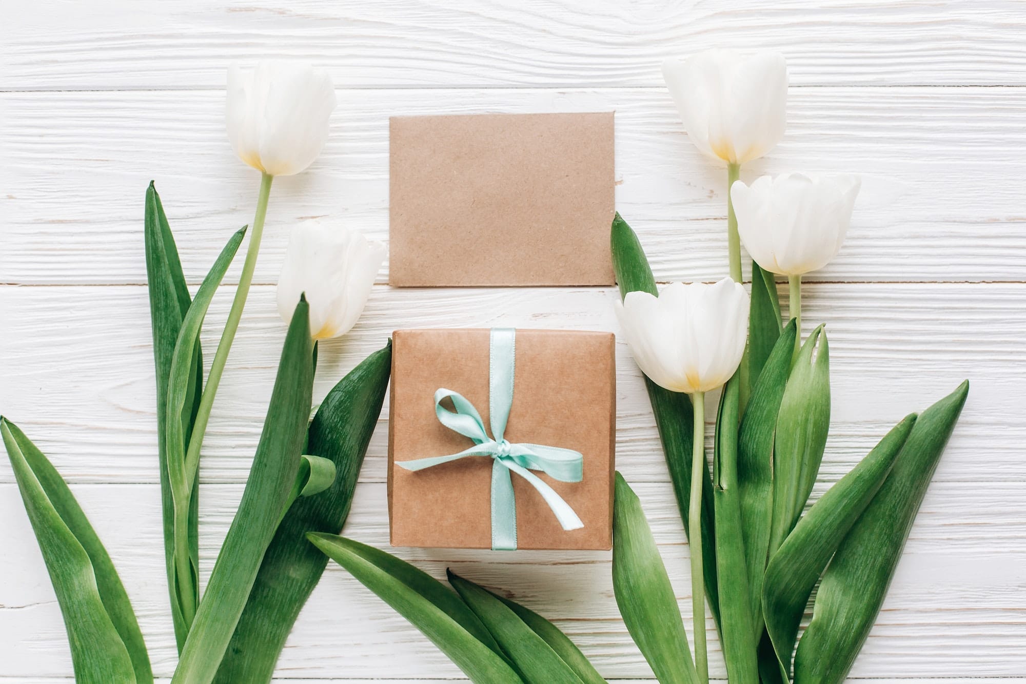 stylish craft present box and tulips on white wooden rustic background